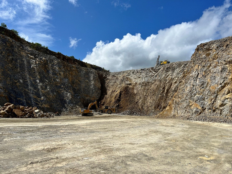 Kalksteintagebau Mühlental-Nord - Das Bild zeigt Felswände eines Kalksteintagebaus, unterhalb der Felswand lädt ein Radlader gesprengtes Haufwerk, daneben steht ein Bagger mit Reißzahn, oberhalb der Felswand arbeitet ein Bohrgerät.